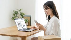 自宅のリビングでくつろぎながら、スマートフォンやパソコンを使ってチャコット下地をオンラインショッピングで探す日本人女性。24時間いつでも注文でき、自宅まで届けてくれる通販は忙しい時の強い味方だ。