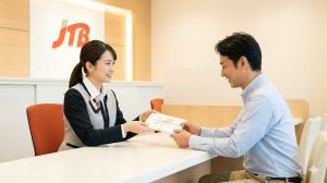 JTBの実店舗で、スタッフから包装されたギフト券を受け取る日本人男性。